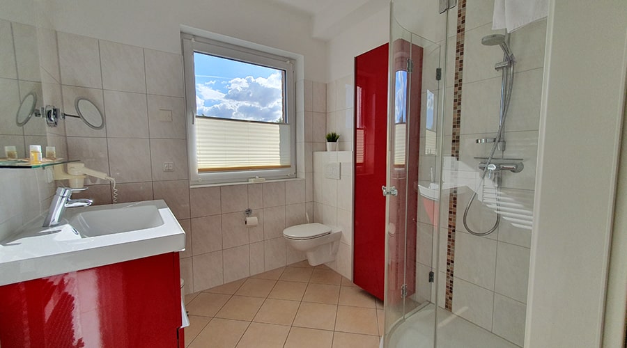 Badezimmer mit rotem Waschbeckenunterschrank, Spiegel, Handtuchheizkörper und Glasdusche